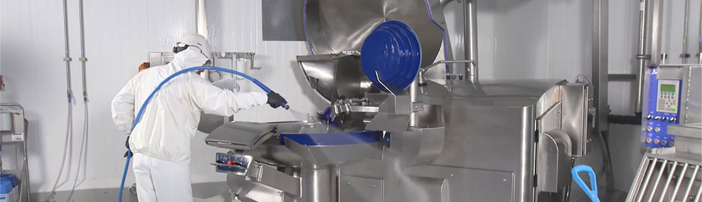 Worker rinsing an industrial cutter in a meat plant